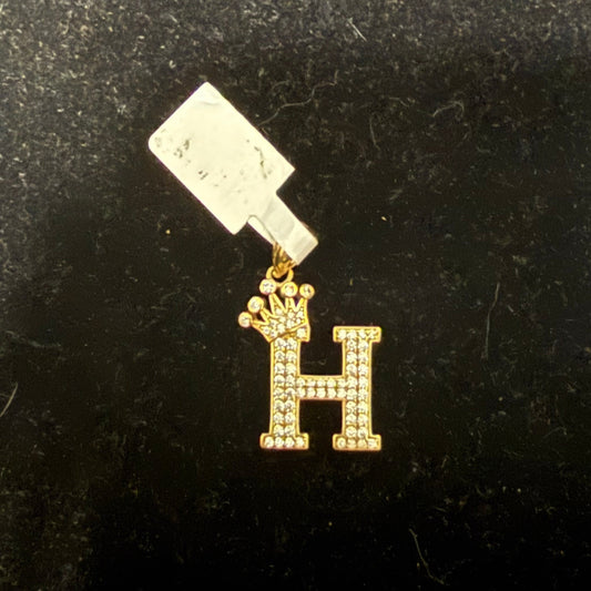 A gold-colored letter 'H' pendant with a clear crystal charm attached to it, displayed against a black background.