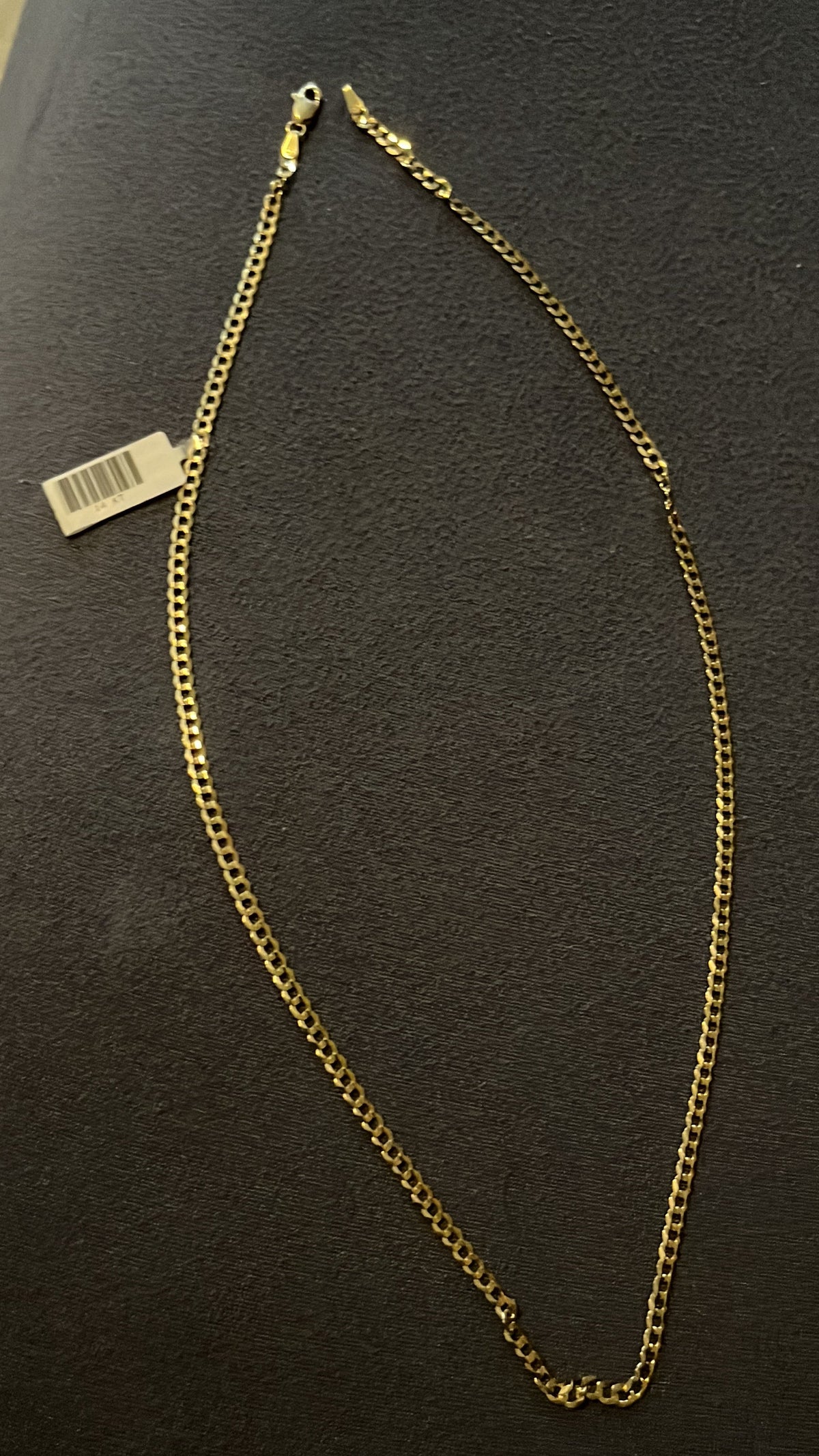 A gold-colored chain necklace with a tag attached, laid out on a textured surface.